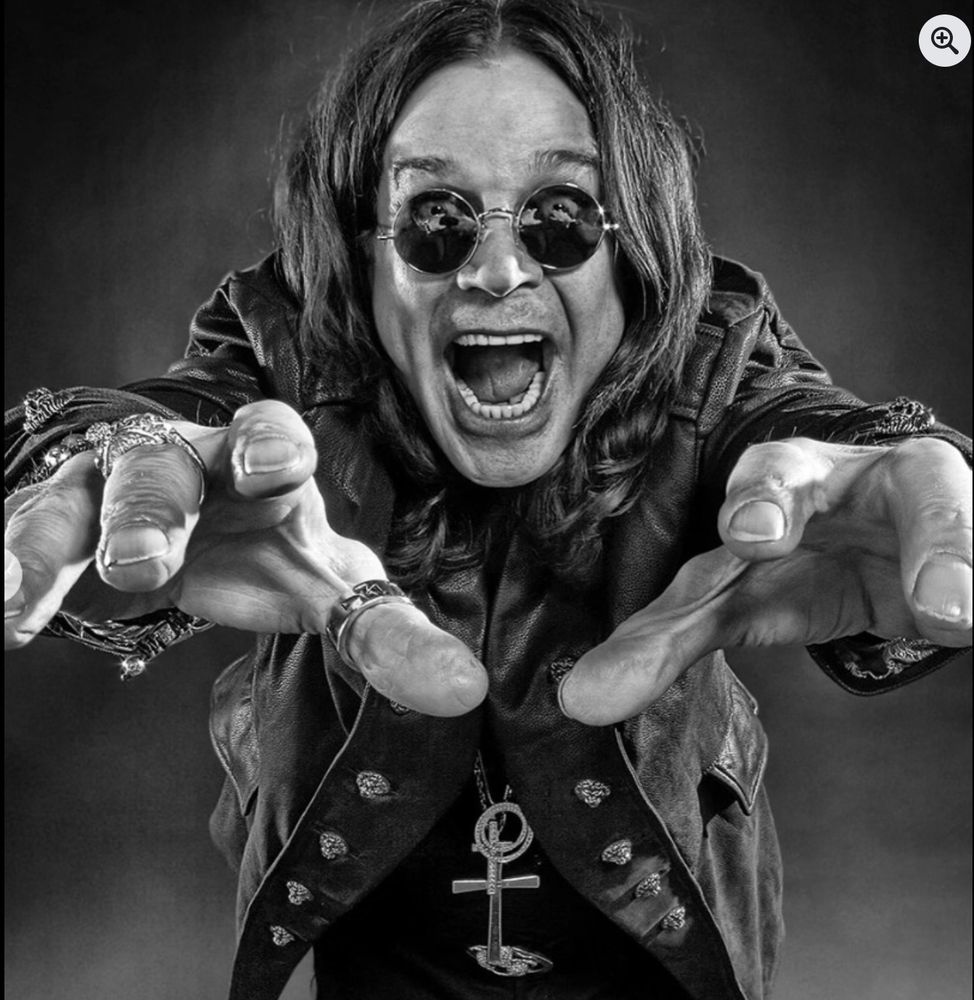 Ozzy Osbourne wears a leather jacket and sunglasses, reaching out to the camera