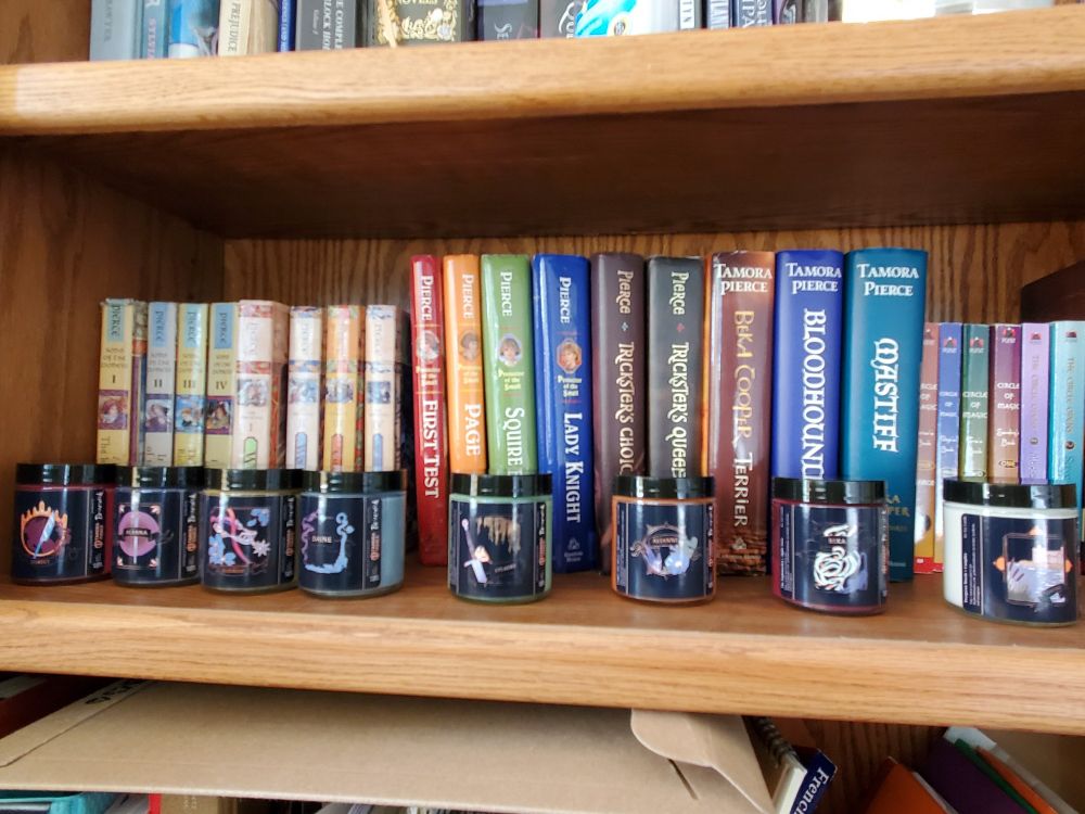 Officially licensed Briarwick candles on a bookshelf full of their respective Tortall series by Tanora Pierce 