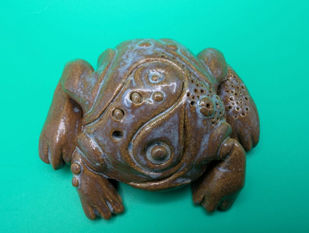 A round stoneware ceramic sculpture of a featureless frog.  Its body is instead carved with vaguely ritualistic symbols.