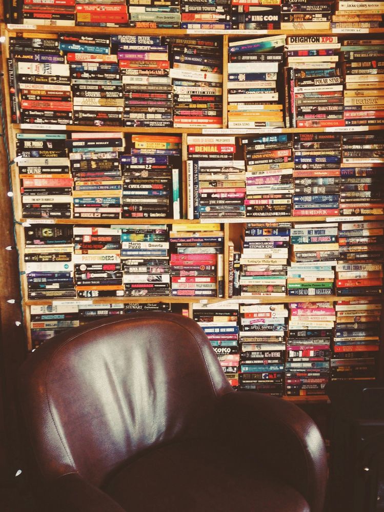 A leather chair in front of a wall of paperback books. Photo by John Salvino on Unsplash.