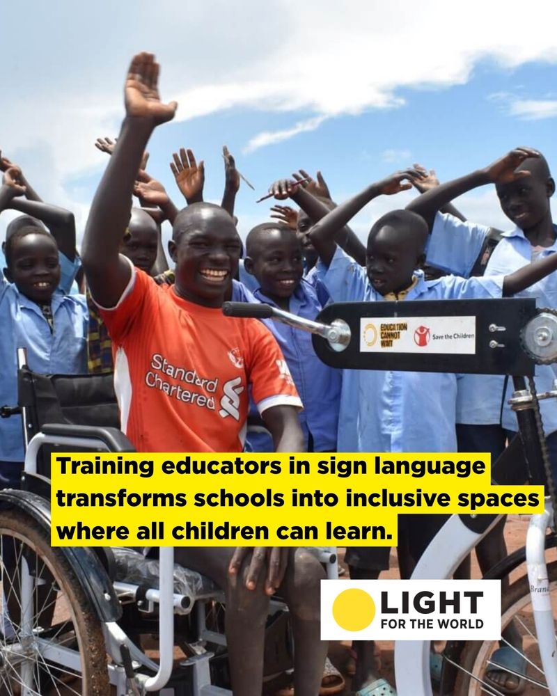 Moses on his new tricycle surrounded by his classmates. Moses has his arm raised and is smiling. His classmates are also smiling.
