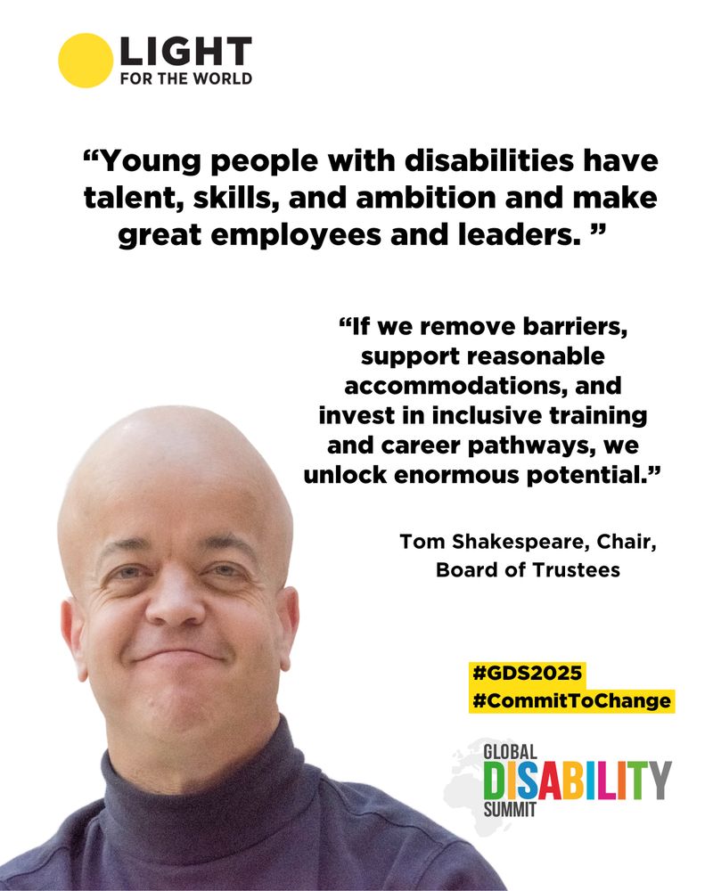 A headshot of Professor Tom Shakespeare. He is a white man, wearing a blue shirt, in this picture. He has blue eyes. Likewise, he smiles at the camera. Tom has achondroplasia.