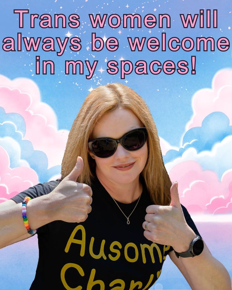 Photo of Charlie wearing a black t-shirt with Ausome Charlie in gold letters, dark cat-eye sunglasses and a Progress Pride bracelet her kid made. She is smiling, both thumbs up. Background is pink and blue stylised clouds, with a blue sky and pink stars. Pink text in the sky says: Trans women will always be welcome in my spaces!