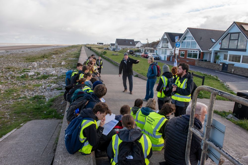 Group of students wearing hi-vis listening to an explanation on a sea wall