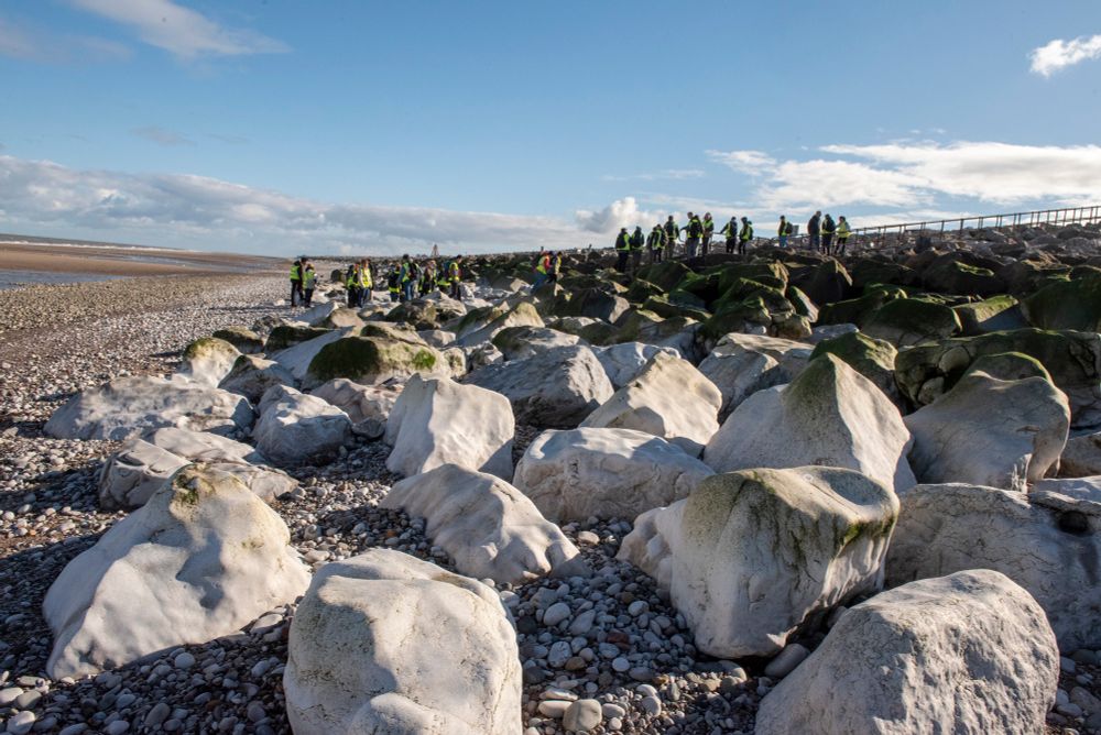 White boulders forming sea defences on a beach with a group of students in the background