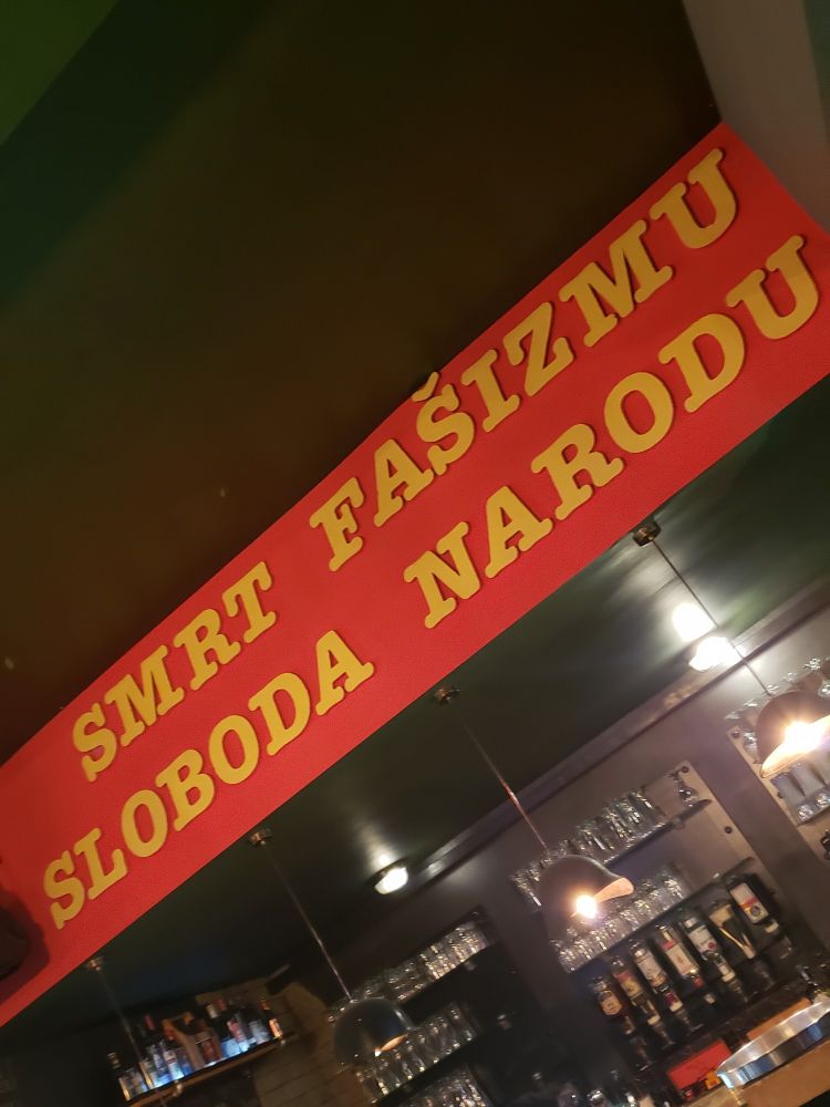 A large sign above the bar in a cafe. Yellow letters on red background: "Smrt fašizmu, sloboda narodu"