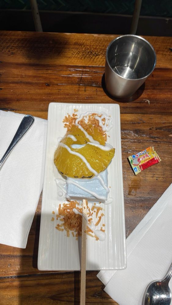 grilled pineapple slice served on blue coconut ice cream with toasted coconut flakes on a narrow white rectangular plate 