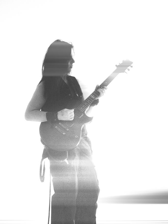 A high key black and white photo of Kiri Bereznai of the post punk rock band, The Rapid Onset. Kiri is dressed in black, awash with rays of light, playing an Ibanez ART300 Blackburst Caiman. 