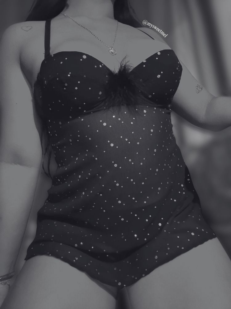 Melody is in a black slip dress adorned with sparkles and feathers.