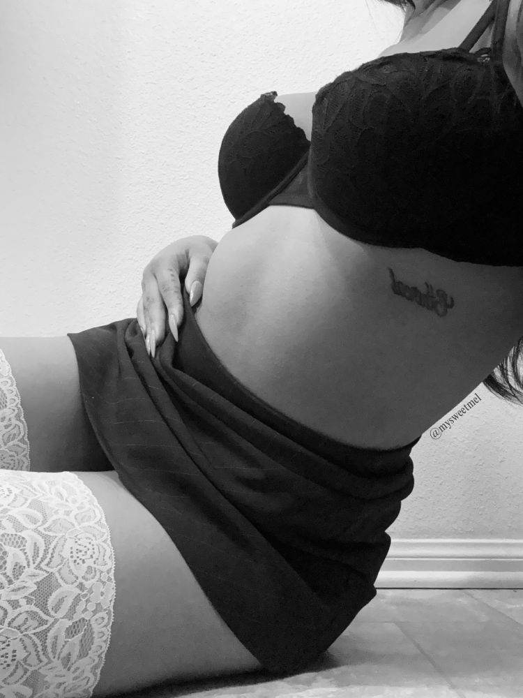 Melody in monochrome, wearing a brown, striped mini skirt and a black lacy bra, paired with lacy white thigh highs. The image only shows the tops of her thigh highs, and cuts off at her neck. She is posed on the floor, with her body slightly angled away from the camera.