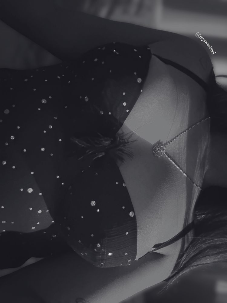 Melody is in a black slip dress adorned with sparkles. This is a close-up of her chest.