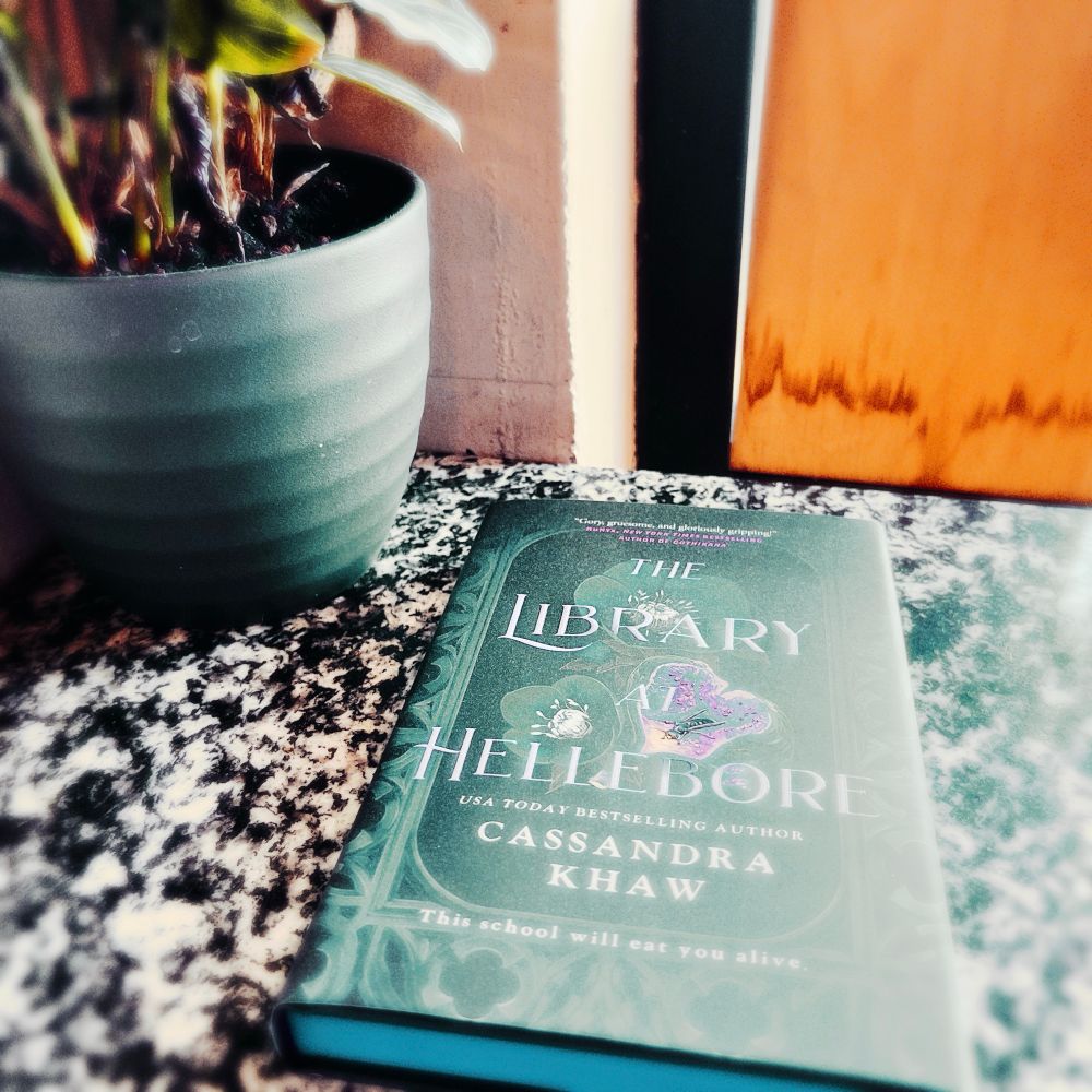Cassandra Khaw’s ‘The Library at Hellebore’ on a marble top beside what I sincerely hope is not a member of the hellebore genus.