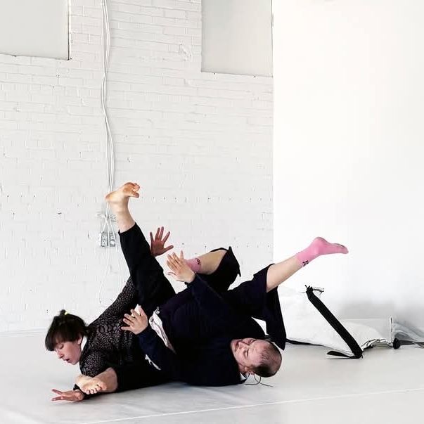 White dance studio and white floor, two dancers, Nate and Lauren dressed in nearly black clothes, entangled with their limbs sticking out Willy nilly so you can make heads or tails of whose limb belongs to who