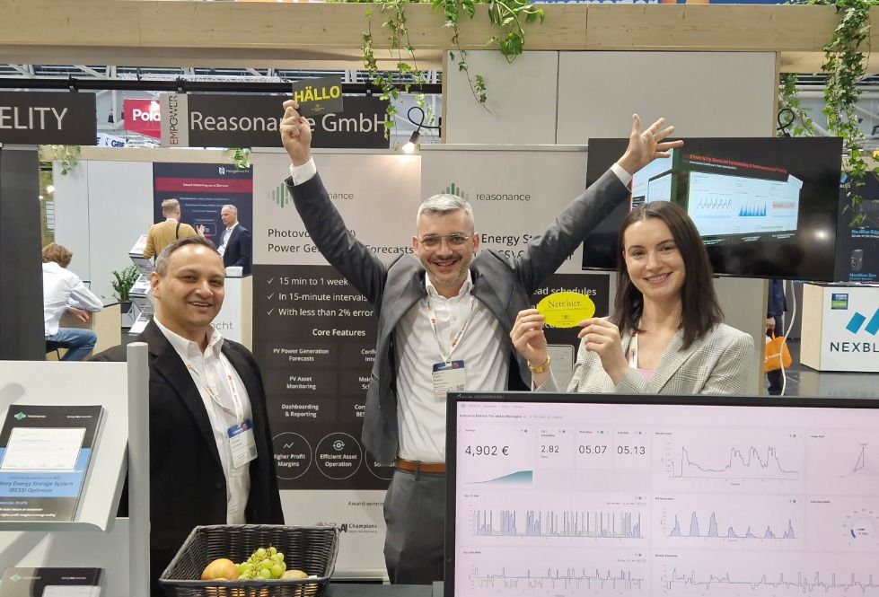Gruppenfoto an einem Messestand auf der The Smarter E 2025: Zwei Männer und eine Frau stehen vor digitalen Displays und einem Bildschirm mit Energieverbrauchsgrafiken. Eine Person hält ein Schild mit „HALLO“, eine andere mit „Nett hier“. Im Hintergrund Banner von CYFIDELITY und reasonance GmbH sowie