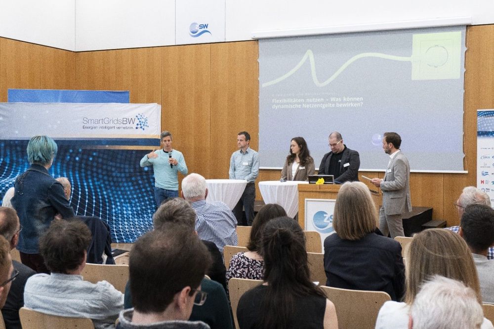 Podiumsdiskussion mit fünf Personen auf der Bühne zum Thema „Flexibilitäten nutzen – Was können dynamische Netzentgelte bewirken?“ im Rahmen der Veranstaltung „§ 14a EnWG und darüber hinaus“. Ein Teilnehmer aus dem Publikum stellt eine Frage.