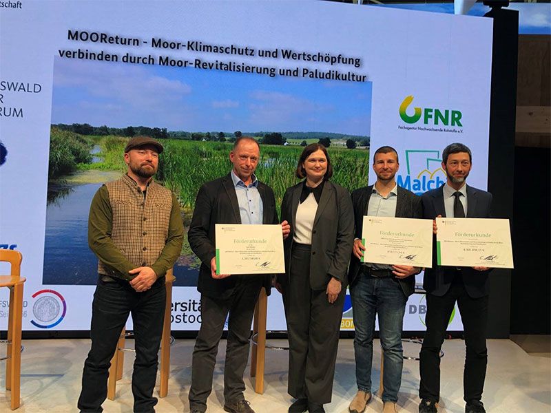 5 Personen auf der Bühne der BMEL-Halle der Grünen Woche. V.l.: Ludwig Borg (Agrotherm GmbH), Axel Müller (Bürgermeister Malchin) PStS Claudia Müller (BMEL), Roman Adam, Volker Lenz (beide DBFZ). 
Foto: FNR
