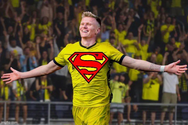 Sam Surridge has his hands open and faces the crowd. A Superman logo is on his jersey.