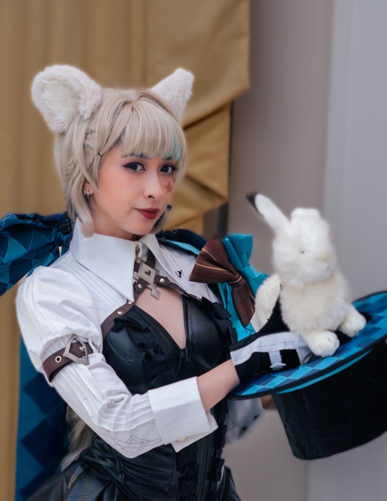 Onyx is dressed as Lynette standing 3/4 to the right while looking at the camera with a half smile. They’re pulling a rabbit out of a magic top hat. 