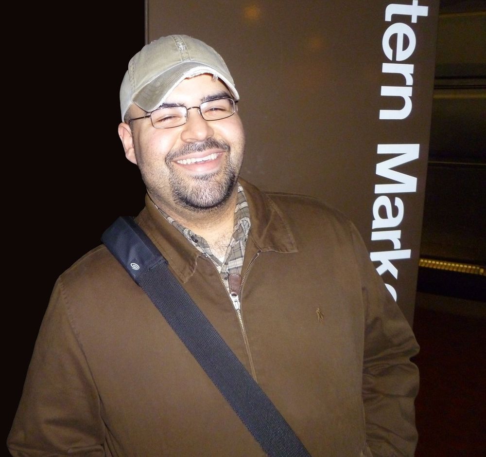 Selfie of Moi wearing a chocolate brown Ralph Lauren jacket and beige cap. Across my right shoulder, lies a TimBuk2 messenger bag strap. I'm smiling but squinting, because of the flash in this picture.