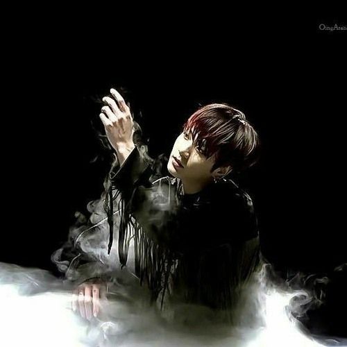 Black background, some white smoke and Jungkook from BTS in a black sweater with frings dancing in MMA 2019.