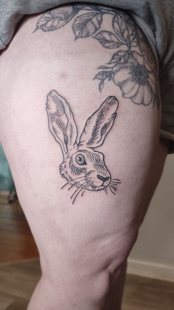 A photo of a fresh tattoo on a thigh representing a hare head. The creature has fangs like a vampire and crosshatching shading.