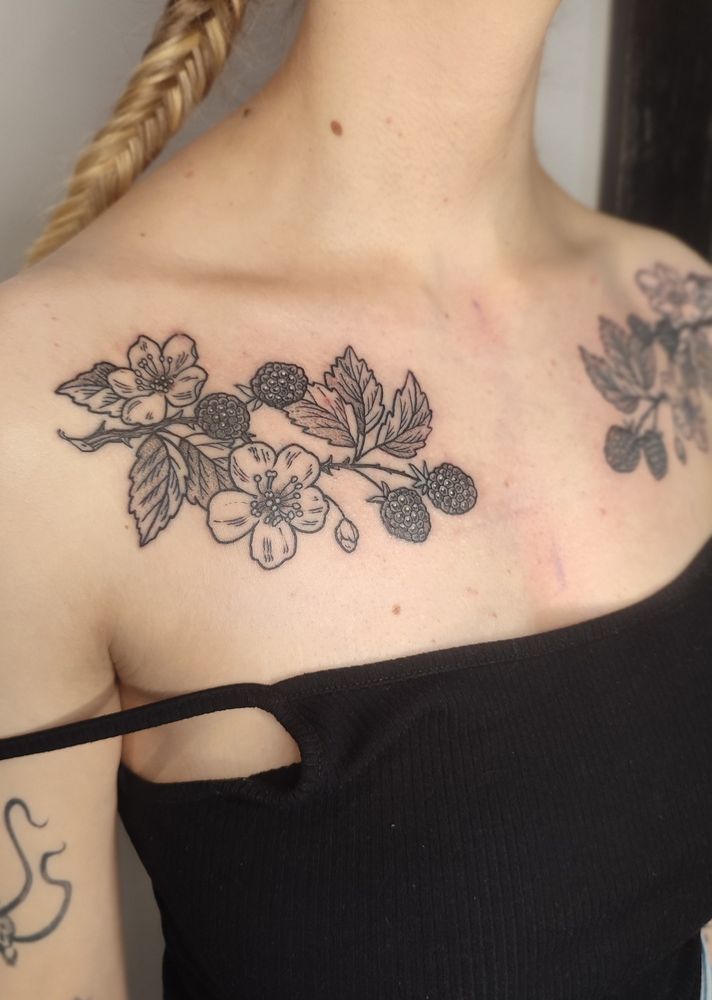 A photo of Bella's chest showing the fresh blackberry branches tattoo, zoomed on the left side. The design contains fruits, flowers, leaves and bud.