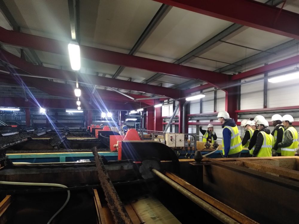 Inside a water treatment works, on the right students are wearing high-vis and hard hats learning about the processes