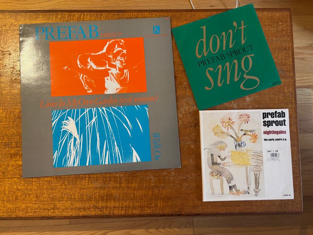 A 4-song 12” Prefab Sprout EP and two 7” Prefab Sprout singles arrayed on one end of a wood coffee table. 