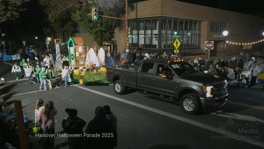 Side view of the parade float from St Joseph Catholic School. It's blurry but appears to have ghosts, jack-o-lantern and possibly a jukebox? With the concentration camp gates at the back