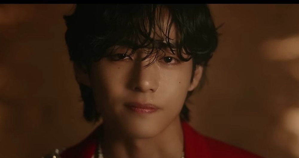 Close up head shot of Kim Taeyhung with a flicker of serene acceptance falling on his face, lips pursed gently, eyes in full contact with his beholder. He wears a structured cranberry red jacket, offset by a soft golden brown background.