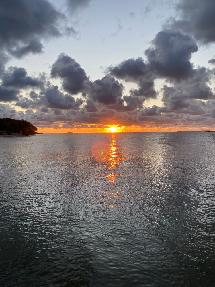A fiery early sunrise over water, with a small bit of tree-covered land visible on the left.