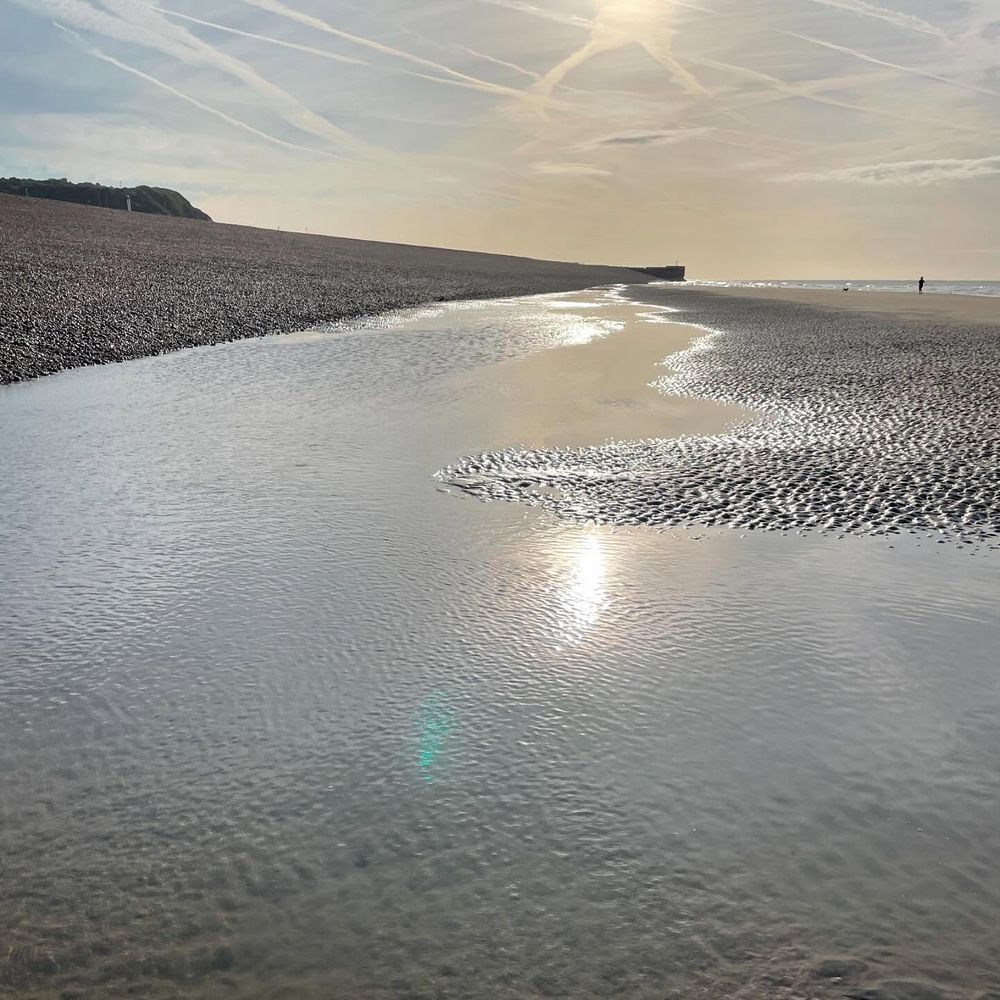 Sun rising over the beach at Hastings at low tide - there's a strip of sand showing with the part nearest the shingle covered in shallow water while the bit nearest the sea is raised in tiny damp dunes.