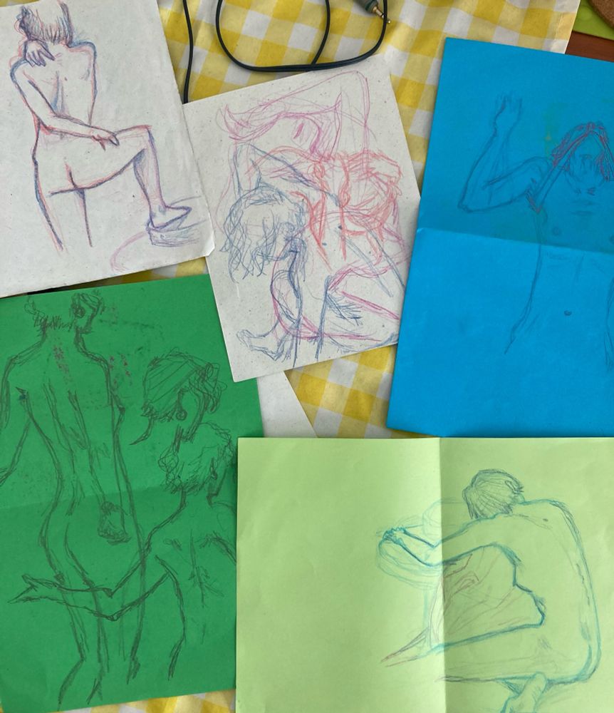 several sheets of coloured paper, some blue some green some white, with drawings of a slim woman with short hair in different poses, done with coloured pencil