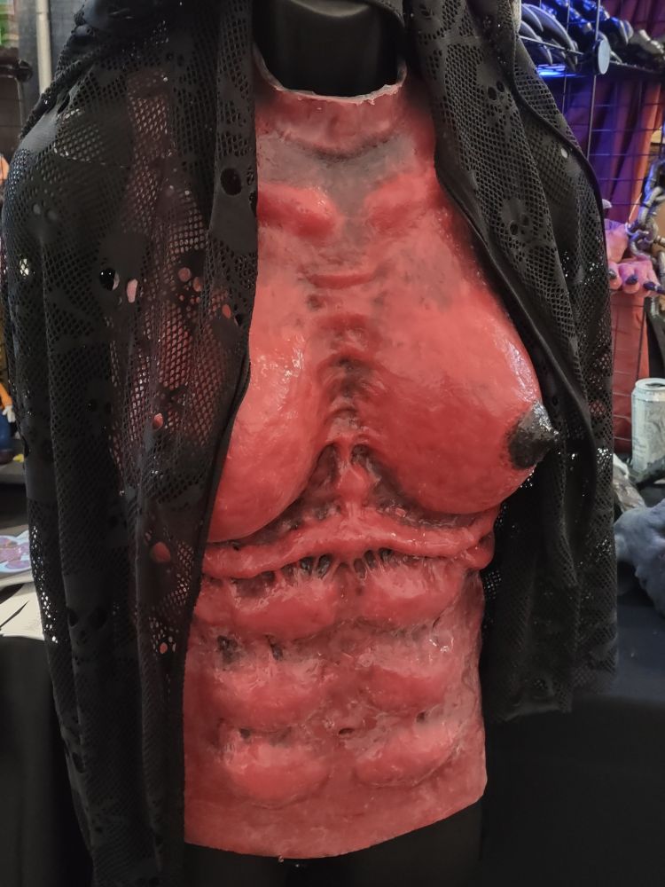 Wearable monster chest made of silicone and painted red with black nipples.  The rib cage is slightly jutting, the tits have a natural sag, the abdomen and collarbone is defined, and there is striation between the pectoral area that would suggest sinewy muscle beneath the fatty breast tissue.