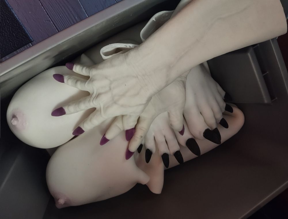 White silicone femsuit with big tits, white silicone monster gloves with purple claws, and white silicone monster feet with black claws displayed in a big tote