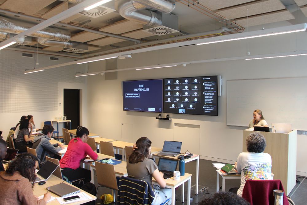 Classroom, a few students are sitting and a female lecturer behind a podium 