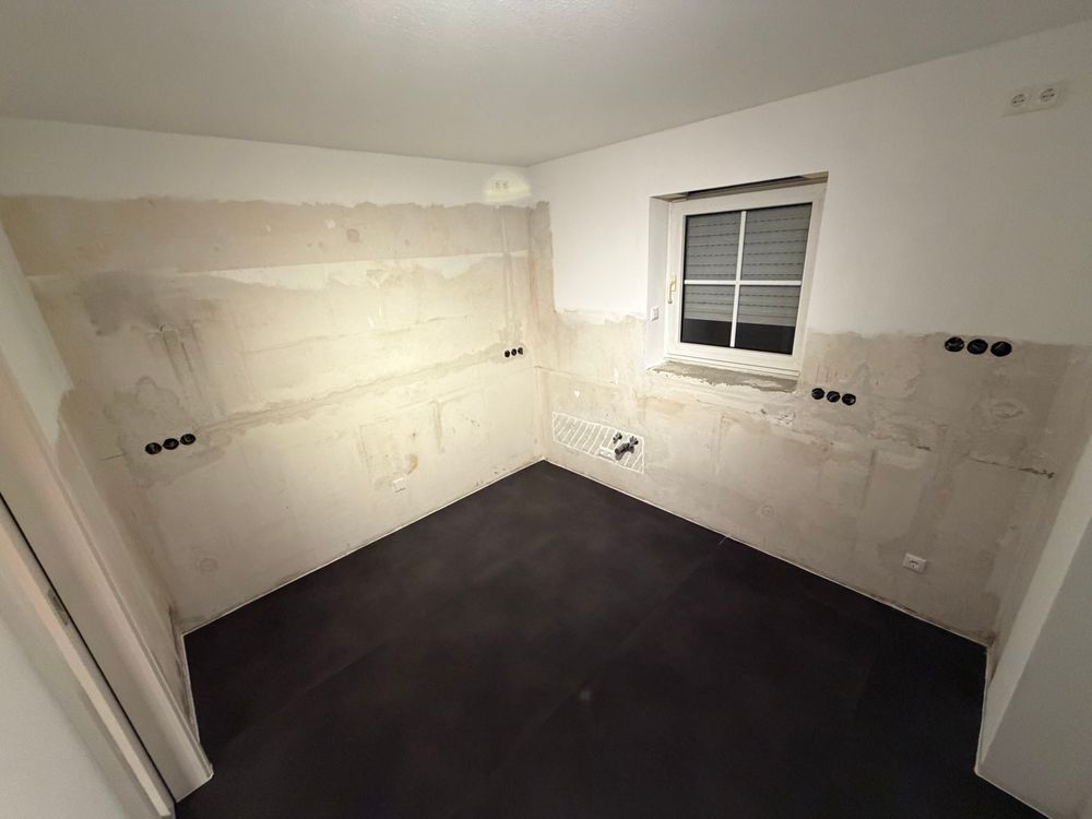 Leeres Küchenzimmer. Dunkler Boden, kahle Wände. 