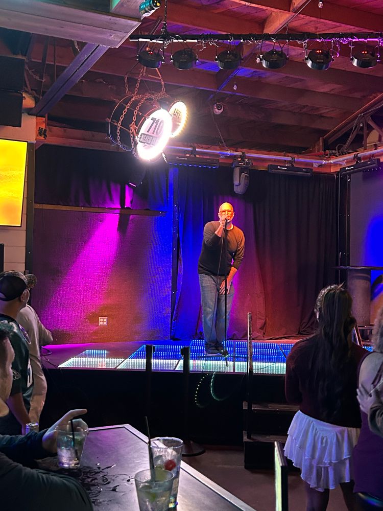 Man singing karaoke on a stage wearing black shirt and jeans 