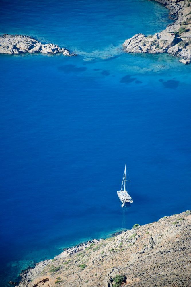 White sailboat anchored offshore on a smooth sea of blue