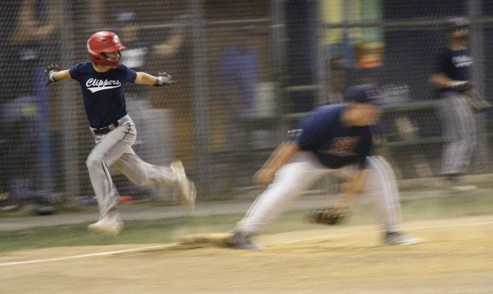 Baseball player in a red batting helmet passing first base making the "safe" signal as a severely motion-blurred first baseman tries to scoop the (late) throw