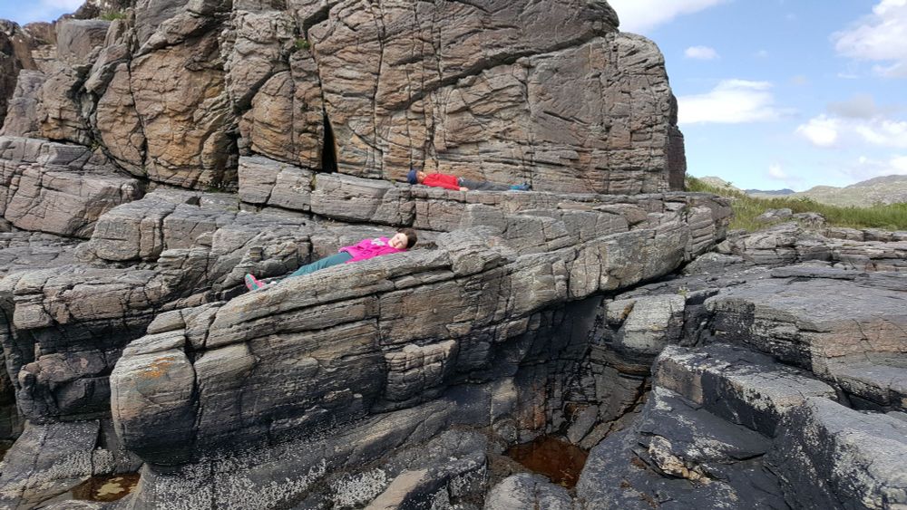 Grey rocky outcrops. Zig-zag folded layers picked out by two children resting on them