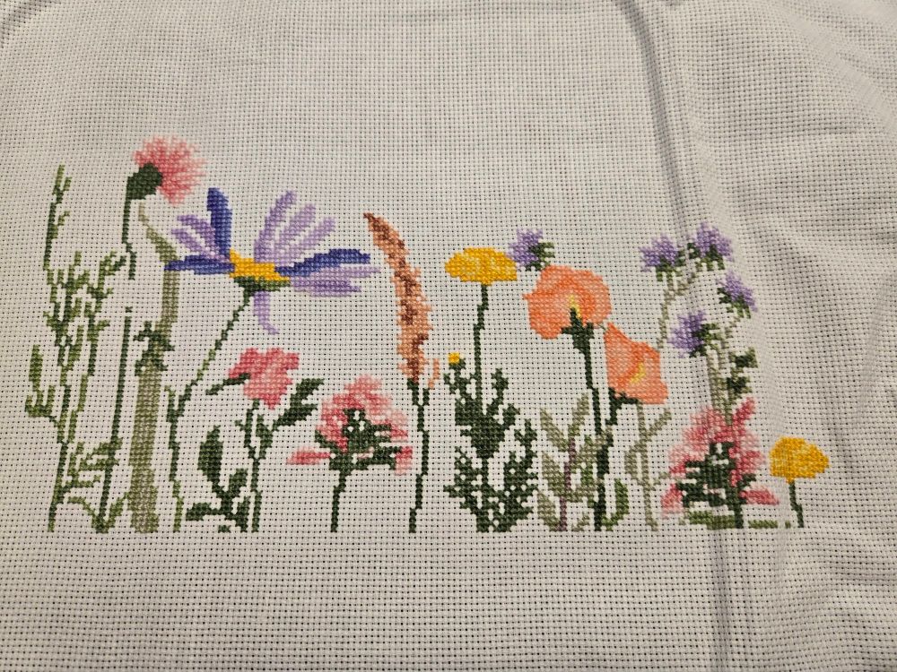 A cross stitch picture featuring purple pink yellow and orange wildflowers on a white background