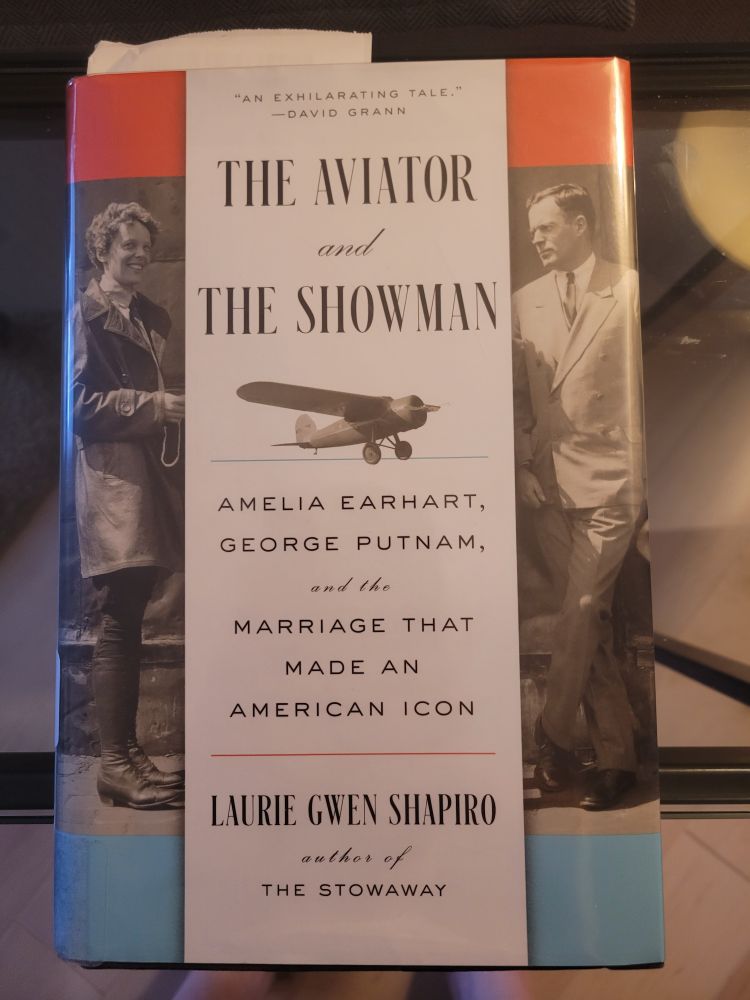 Cover of Laurie Gwen Shapiro's "The Aviator and The Showman". Subtitle: Amelia Earhart, George Putnam, and the marriage that made an American icon. Vertically formatted grayscale images showing Amelia on the left, George on the right.