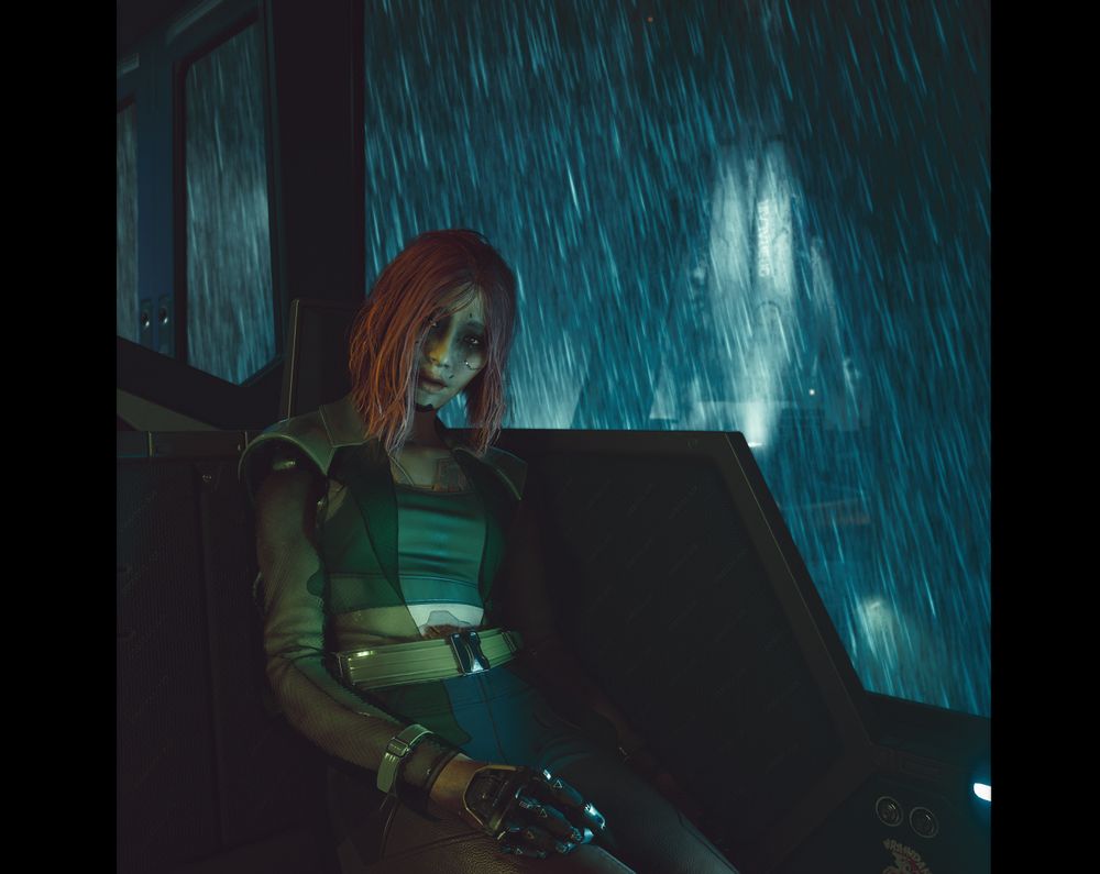 An image of Songbird sitting on the seats of the train, on her way to the launchpad. She is looking up at V (the camera) as she leans slightly to the right. She appears to be in rough condition, the skin around her eyes blackened, her overall complexion ill, her frame almost limp. Despite this, her expression is warm as she smiles at V. The wide windows behind her reveal the rocket preparing for launch, rain pouring down heavily. The image is cropped slightly, made square, with black bars on either side.
