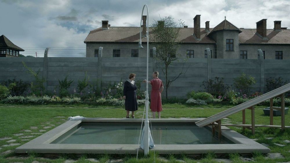 Hedwig Höss and her mother in their garden outside Auschwitz, discussing whether their former neighbor, a Jewish woman, was inside after she was arrested and dispossessed. Hedwig's mother explains that her belongings were auctioned off by the state.