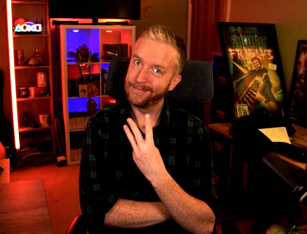 Red-headed Irish/British man RedWeird posing in front of his stream room, holding up three fingers to indicate how many nights a week he will be live again