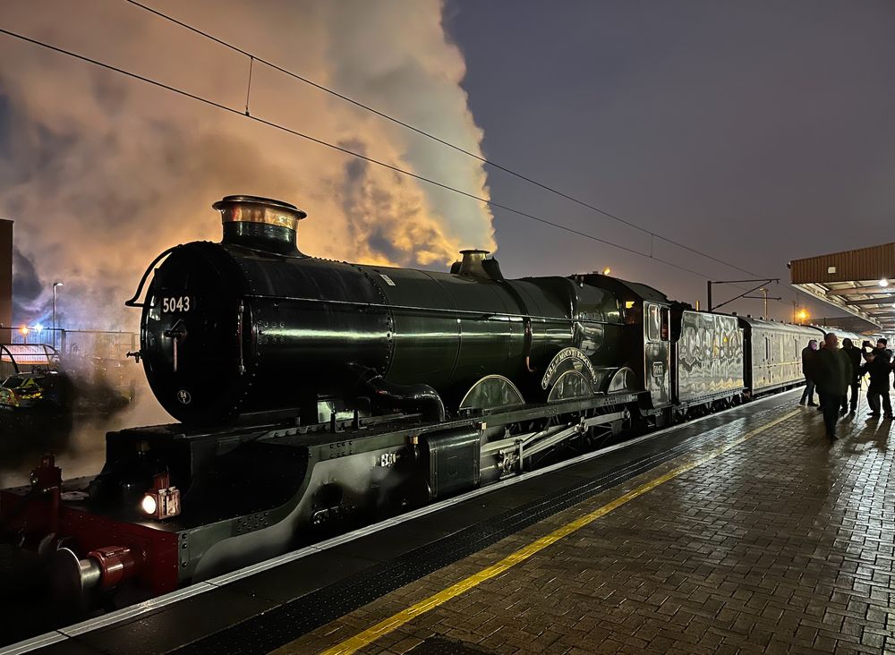 It's a damp twilight evening. We're at a railway station looking at a steam engine called 'Earl of Mount Edgcumbe', a GWR Castle class locomotive  built in 1936. It's painted a rich deep green colour and the steam coming from the regulator valve is tinged pink by the twilight.
