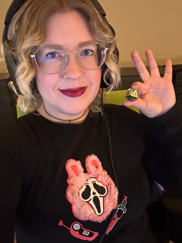 Jennifer wearing a shirt with a pink fuzzy Ghostface with bunny ears, holding a D20