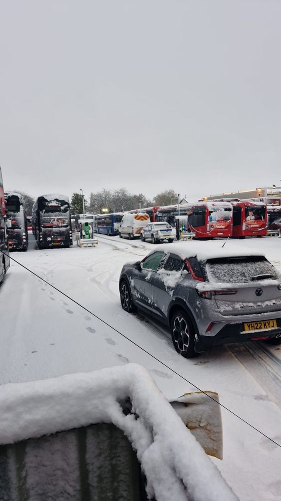 Rows of buses parked up in a snow covered depot.