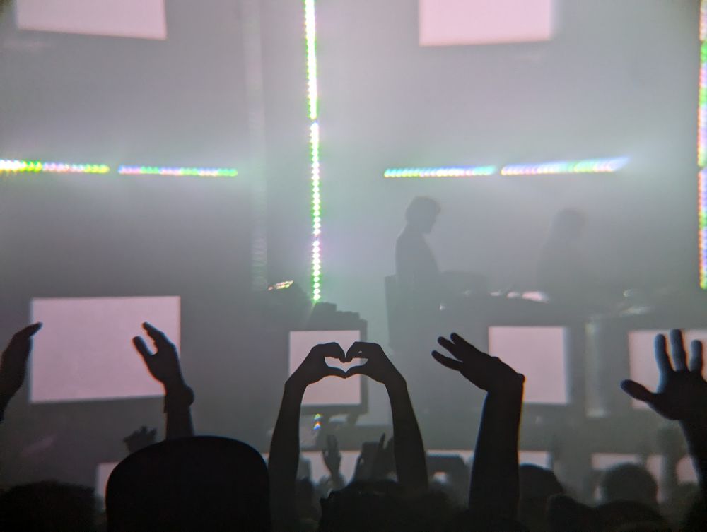 Justice performing in Vancouver in 2024, with fans holding up hands in the shape of a heart in the foreground.  